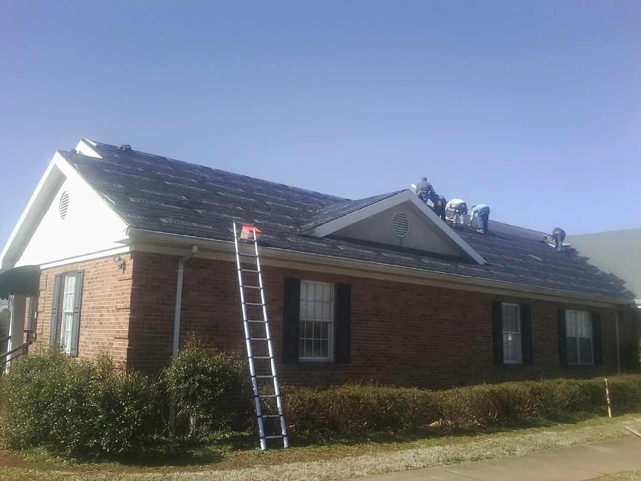 Crew tearing shingles off a brick ranch roof with a ladder set — Metal Roof Repair work by our crew in Waverly